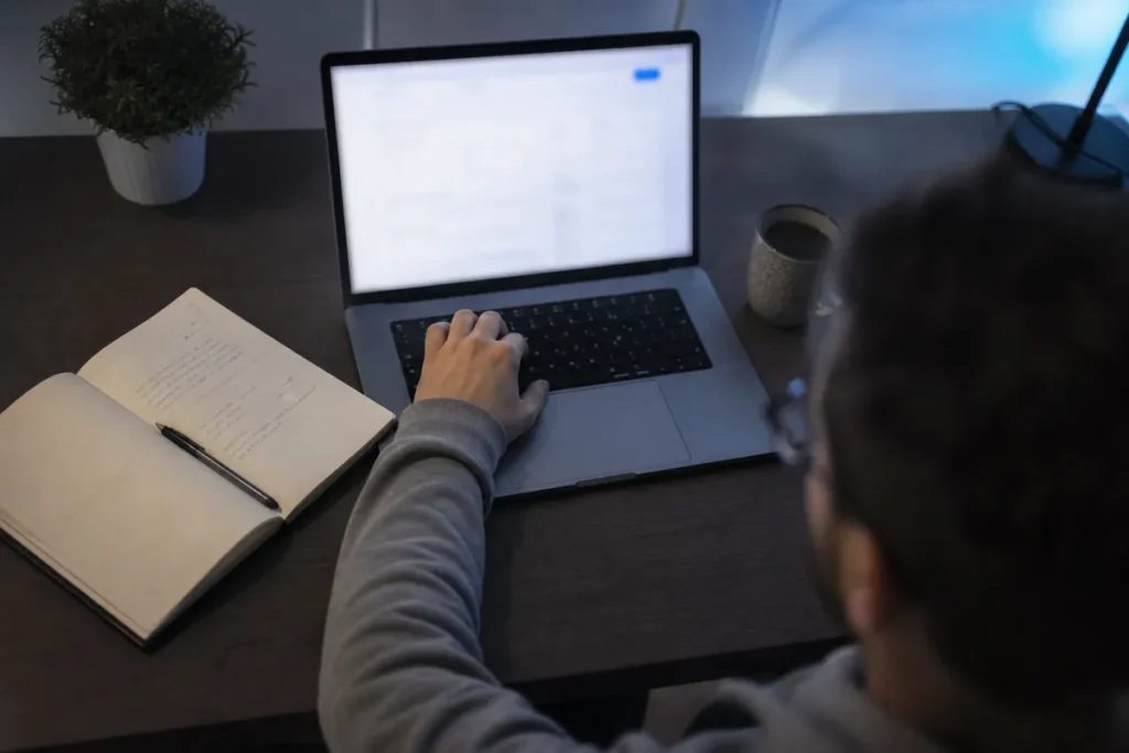 Estudante preenchendo a inscrição do Sisu no notebook, com caderno de anotações ao lado