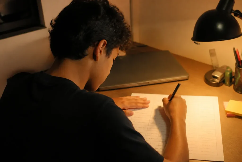 Quando começar a estudar para o Enem: estudante montando o cronograma semanal numa folha, à luz de luminária (foto 936 mantida do post)