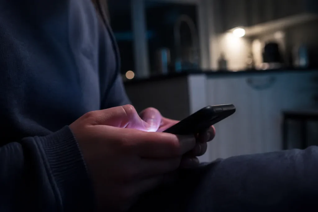 Mãos de estudante segurando o celular à noite para consultar a nota na Página do Participante do Enem