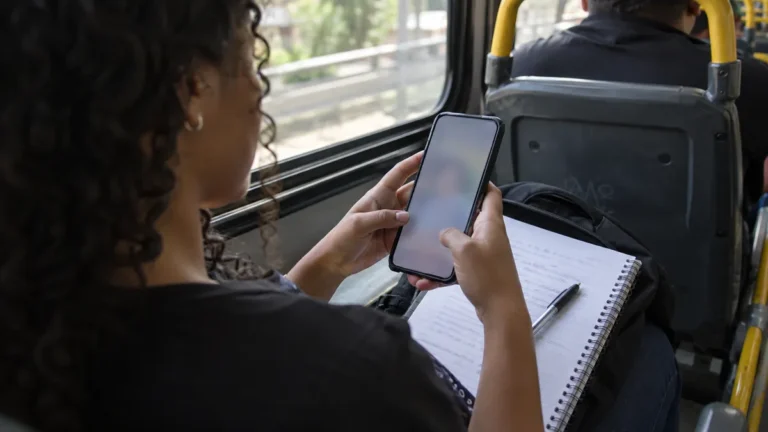 estudar pelo celular numa mesa de cozinha vista de cima, com o aparelho aberto numa prova em PDF ao lado de um caderno
